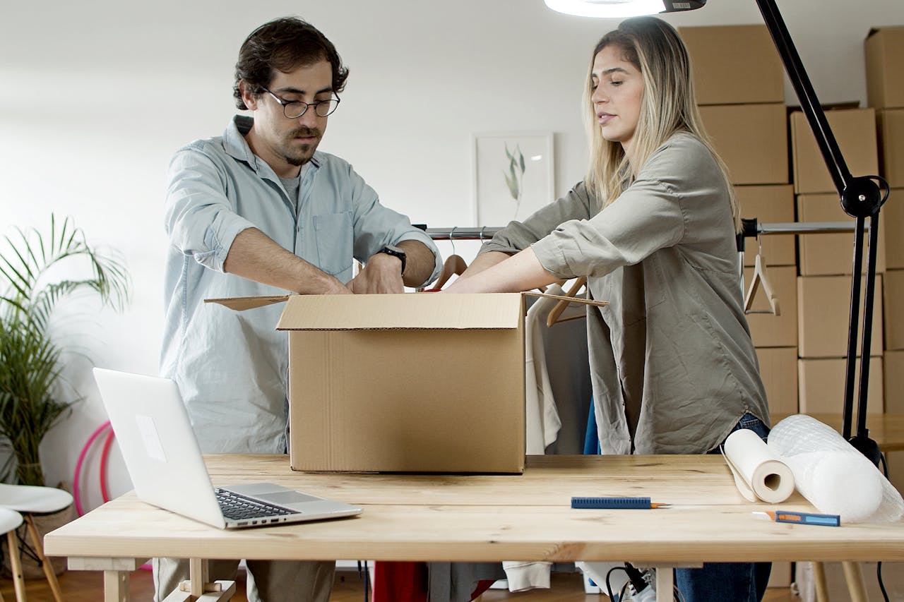 Man and woman packing e-commerce orders at startup business with laptop and boxes indoors.